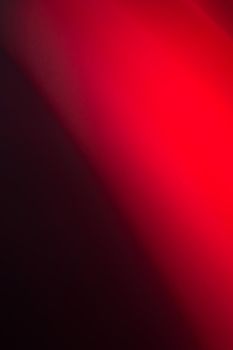 Bright red light on a black vertical background. Abstract backdrop.