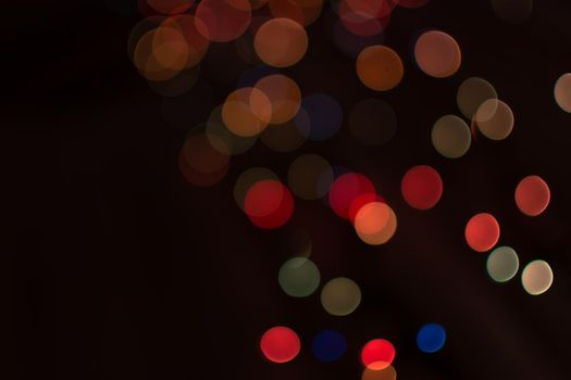 Multicolored bokeh from light garlands on a dark background. Festive background.
