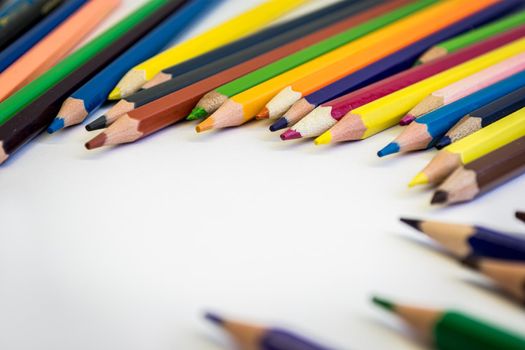 Colored pencils on a white table are scattered in a semicircle with space for text.