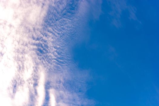 Small cirrus clouds illuminated by the sun against a blue sky at sunset.