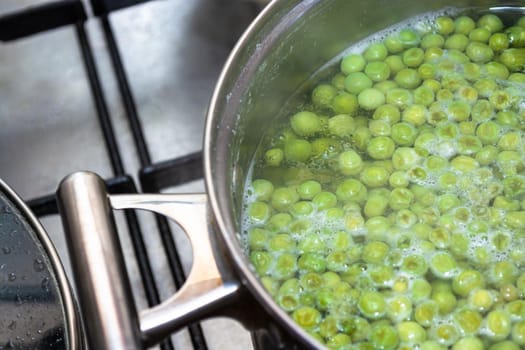 Cooking green peas in a metal pot on a gas stove. Boiling. Culinary theme.