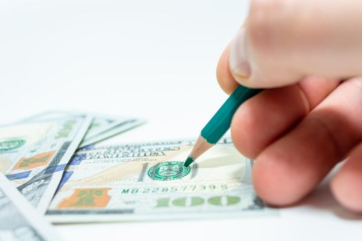 Draw to counterfeit money. A bang in hand holds a pencil over a hundred dollar bill. Selective focus. White background.