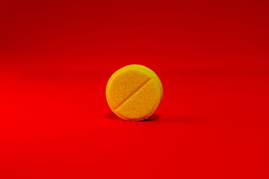 Yellow one pill on a bright red background close-up. Place for your text. Selective focus. Healthcare and medical concept.