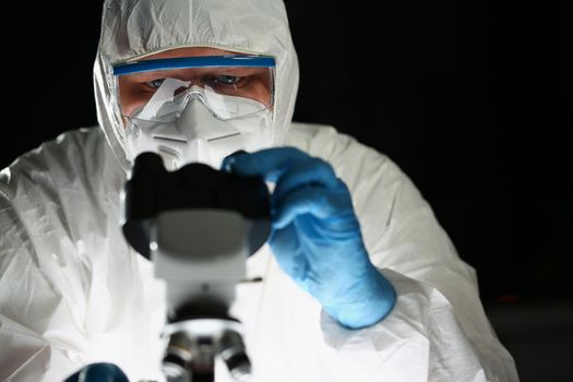 Close-up of concentrated person chemist in blue protective gloves look at microscope in chemistry laboratory. Scientist testing unique sample. Lab concept