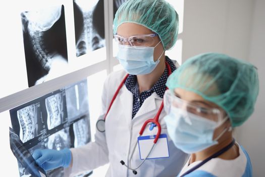 Portrait of women professional doctors look through x ray scans in hospital, examine patients result. Colleagues in protective uniform. Medicine concept