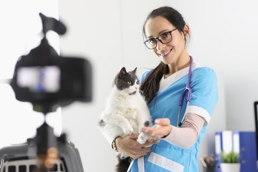 Portrait of female doctor present cute kitty on camera, petting him for video. Prepare for animal exhibition, live show, social media. Veterinary concept