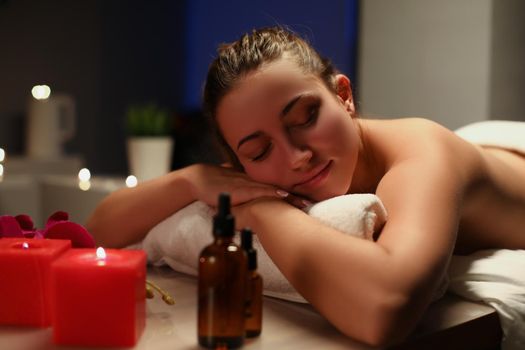 Portrait of young happy girl lay with closed eyes on massage table in spa. Lady enjoy relaxation in luxury spa centre. Massage, wellness, self love concept