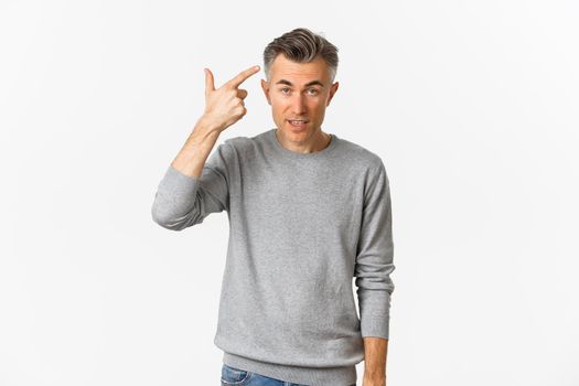 Image of skeptical middle-aged man scolding someone for stupid mistake, pointing finger at head and looking annoyed, standing over white background.