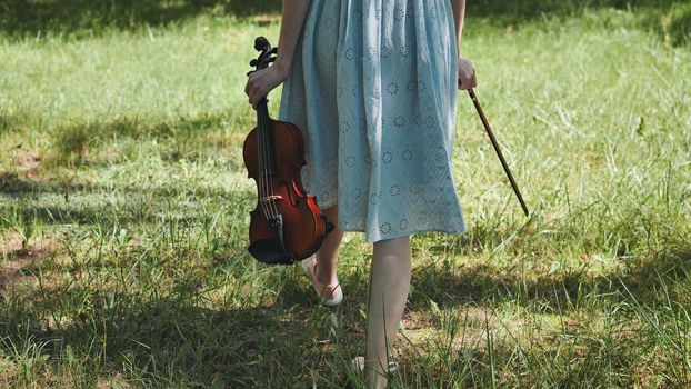 A girl in a dress walks with a violin in a city park
