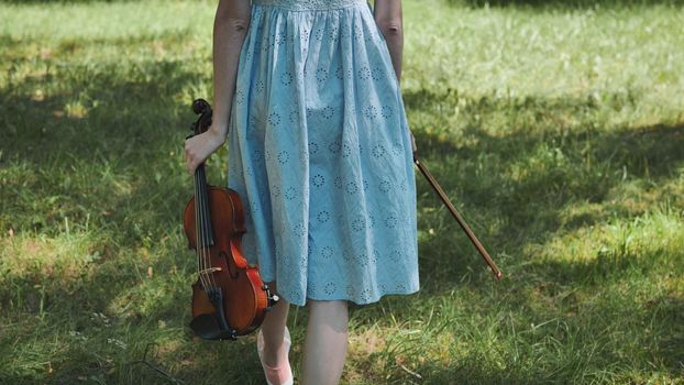 A girl in a dress walks with a violin in a city park