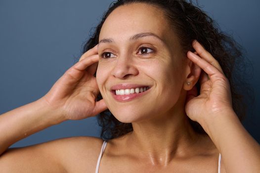 Close-up portrait of middle aged woman with no make-up and wet skin smiles toothy smile while washing her face, taking care of her beauty and skin. Freshness, purity, cleanse, removing make-up concept