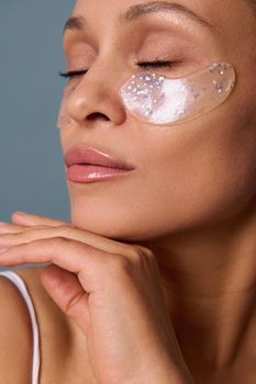 Close-up of the face of a beautiful woman with perfect glowing skin and natural makeup posing for camera with medical collagen patches under her eyes to reduce fatigue and puffiness. Skin care concept