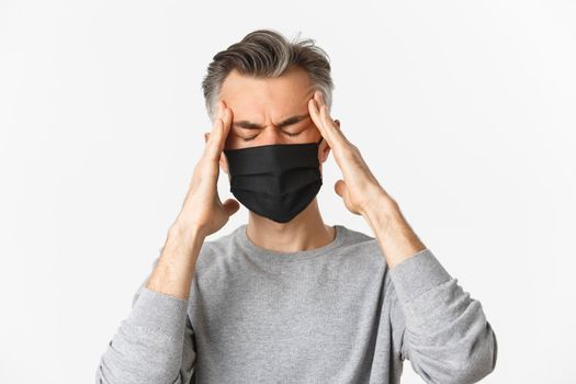 Concept of covid-19, social distancing and quarantine. Close-up of middle-aged man in medical mask, feeling sick or dizzy, touching head, suffering headache or fever from coronavirus.