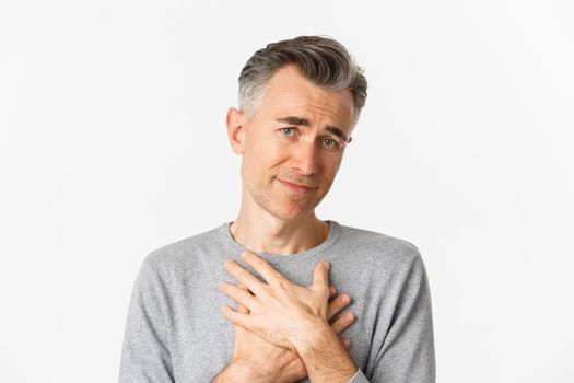 Close-up of thankful middle-aged man, holding hands on heart and feeling touched, appreciate kind gesture, standing over white background.