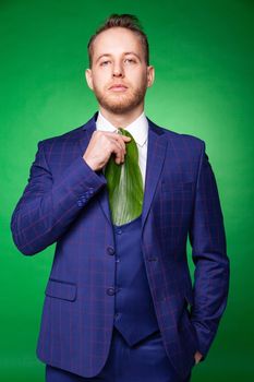 Determined businessman in elegant suit adjusting leaf tie on green background in studio while showing concept of ecology and looking at camera