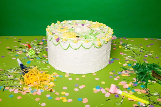 High angle of delicious birthday cake placed on green table with confetti and party horns in studio