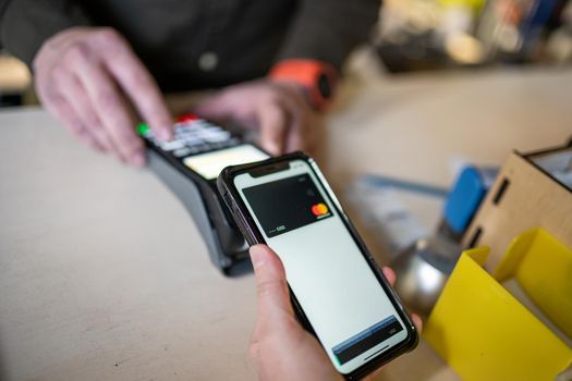 Shopping with mobile phone payment. Customer using contactless payment. Female hand paying with NFC technology on phone. Paying contactless with digital wallet. Pay by card on NFC payment terminal.