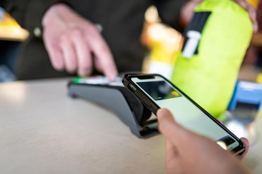 Shopping with mobile phone payment. Customer using contactless payment. Female hand paying with NFC technology on phone. Paying contactless with digital wallet. Pay by card on NFC payment terminal.