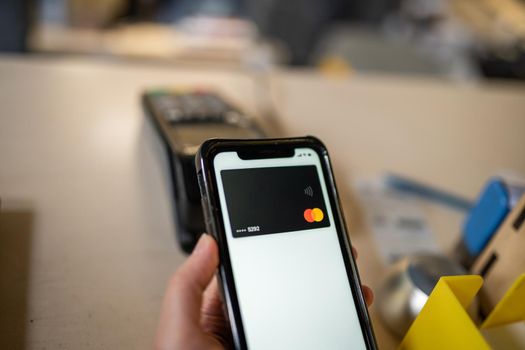 Woman hand paying using NFC technology. Customer paying through mobile phone using contactless technology. Closeup hands of mobile payment. Paying with just a tap. Easy contactless payment system.