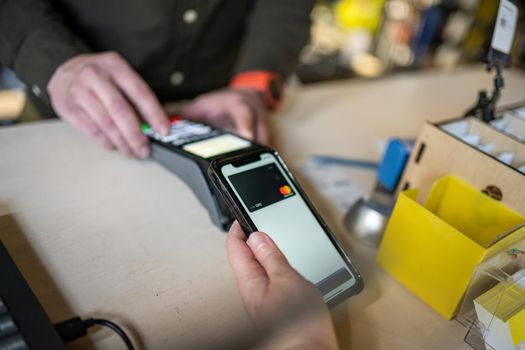 Woman hand paying using NFC technology. Customer paying through mobile phone using contactless technology. Closeup hands of mobile payment. Paying with just a tap. Easy contactless payment system.