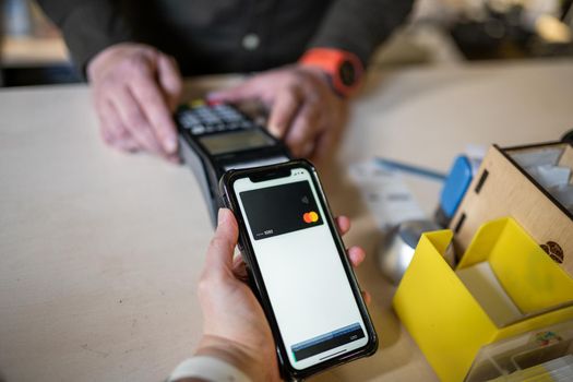 Shopping with mobile phone payment. Customer using contactless payment. Female hand paying with NFC technology on phone. Paying contactless with digital wallet. Pay by card on NFC payment terminal.
