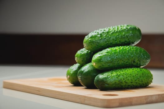 Close-up of several fresh cucumbers lie on a wooden cutting board on a white table. copy space vegetarian food.