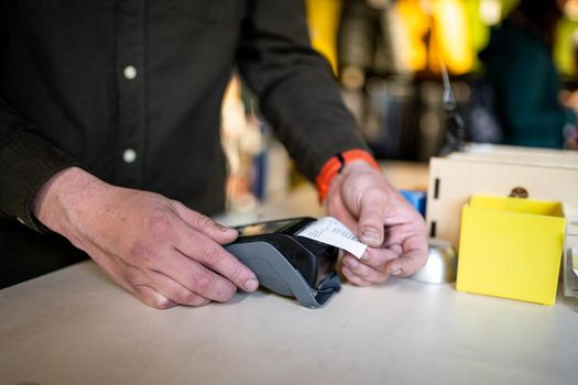 Man holds payment terminal while holding receipt for completing a purchase. Hands close up and side view. Concept of NFC, business and banking transaction. Close up of payment device, card machine.