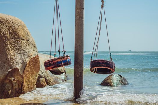 Real Nature Beauty summer ocean landscape background. Hang rope swing old tires paint red blue. Clear Sea blue skyline sand beach water edge yellow rock. Day sun joy fun paradise vacation romantic.