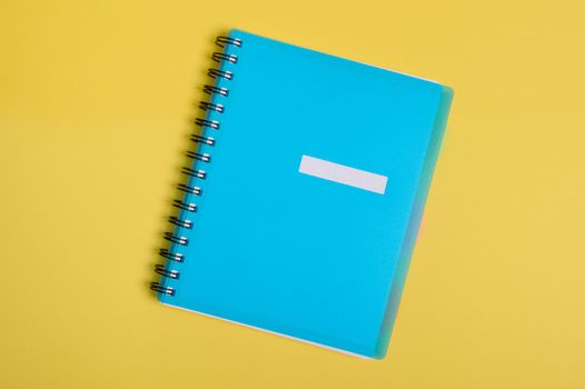 Close-up of a blue colorful organizer, notepad with empty blank sheet for text, isolated on yellow background with copy space. Flat lay of office supply