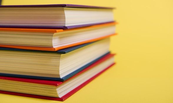 Close-up of a stack of multicolored books on yellow surface background with copy space for text. Teacher's Day concept, Knowledge, literature ,reading, erudition