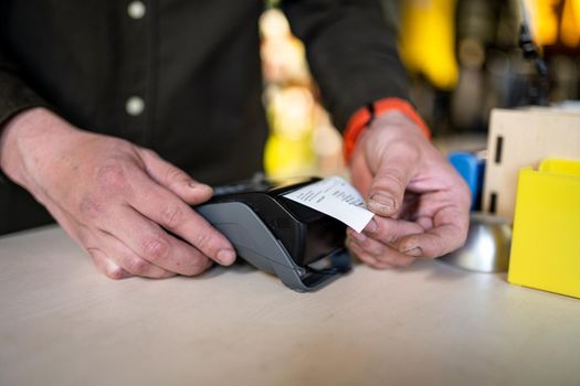 Salesman holds payment terminal while holding receipt for completing purchase. Hands close up. Concept of NFC, business and banking transactions. Payment terminal with paper tape. Bank terminal.