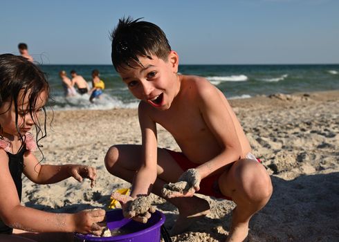 Children playing at the sandy beach. Adorable kids building sandy castles. Focus on handsome funny boy enjoying summer holidays at the island. Summer vacations concept, happy joyful summer holidays