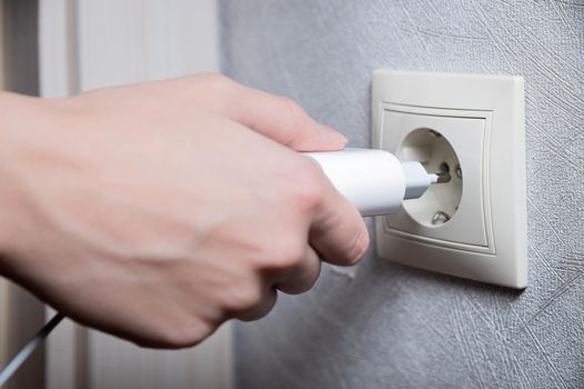 Close-up of a woman's hand inserting a white usb charger into a 220 volt socket.