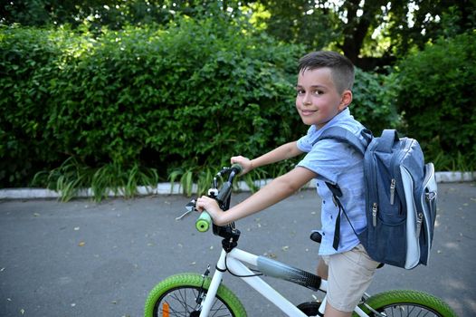 Adorable kid boy with school bag , riding a bicycle cute smiles looking at camera. Back to school concept