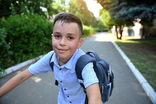 Portrait of handsome school boy with school bag riding bicycle . Child coming back to school