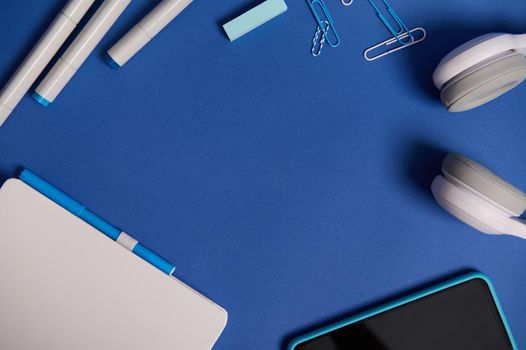 Flat lay composition with white stationery office or school supplies and electronic wireless gadgets scattered in a circle on blue background with copy space. Teacher's Day, Back to school concept