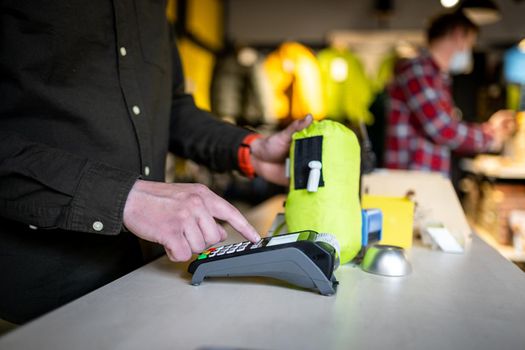 Close-up of the hands of a male salesman cashier holding POS terminal and paper receipt behind the counter of a sports store. Cashless technology and credit card payment concept. Card swipe machine.