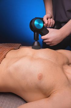 Close-up of a Caucasian male pectoral muscle percussion massager working out in a professional massage parlor.