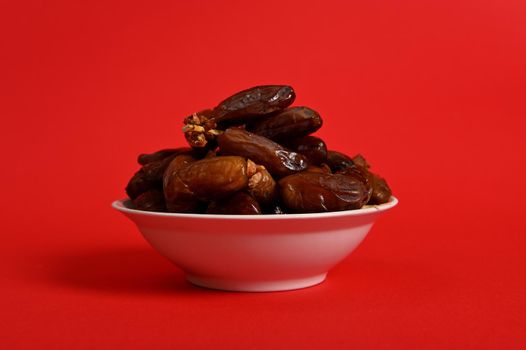 A plate with delicious fresh dates to break the fast in Ramadan, isolated on red background, copy space.