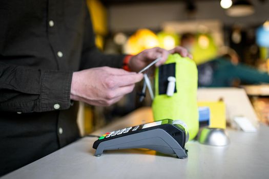 Close-up of the hands of a male salesman cashier holding POS terminal and paper receipt behind the counter of a sports store. Cashless technology and credit card payment concept. Card swipe machine.