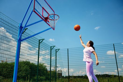 Young woman playing basketball on the court and throwing the ball into the hoop. Motion, active lifestyles concepts.