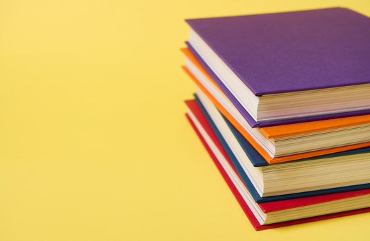 Stack of multicolored books on yellow surface background with copy space for text. Teacher's Day concept, Knowledge, literature ,reading, erudition concepts