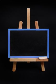 Close-up of a chalk blackboard with empty space for text, standing on a wooden table easel isolated on black background with copy space.