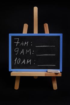 Close-up of a blackboard on a wooden table easel, with lettering schedule with a white chalk isolated over black background with copy space. Planning concepts, time management, timetable and timing.
