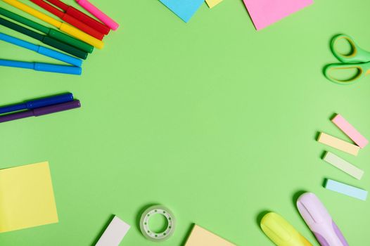 Flat lay composition with stationery office or school supplies scattered in a circle on a light green background with copy space. Back to school concept. High angle view