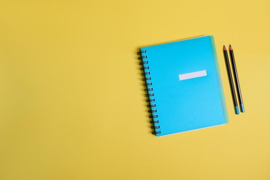 Blue colorful notepad, organizer and two pencils, on yellow background with space for text. Back to School and Teachers' Day, office and business, time management, planning concepts. Flat lay