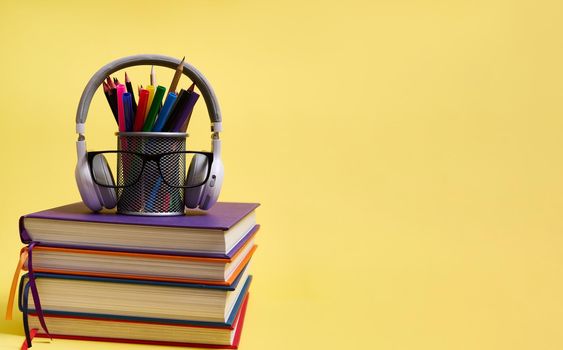 Back to school concepts. Teachers Day. Composition from a stack of books pencils glasses wireless headphones on a yellow background with copy space