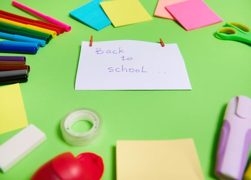 Soft focus on a white paper with lettering Back To School in the center of multi colored assortment of stationery office supplies and school accessories arranged in a circle. Copy space