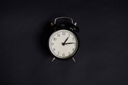 High angle view of a monochrome composition with a vintage alarm clock on black background with copy space . Back to School and Teachers Day Concepts, Business, Organization, Time Management. Flat lay. Top view