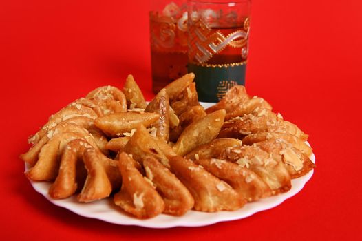 A plate with Arabian dessert from almond flour and honey and two beautiful glass with traditional Moroccan tea with mint on red background with copy space